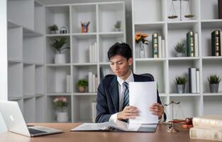 Young professional in suit examining documents at desk, focused on analysis and decision-making in modern office. photo