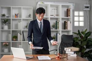 Young businessman expressing concern while reviewing documents in a modern office setting. photo