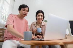 Senior couple enjoying coffee while exploring content on a laptop at home. photo