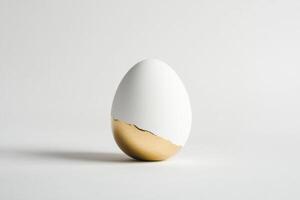 White egg with gold bottom half standing on plain background reflects art concept photo