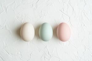 Three pastel-colored eggs arranged on textured white background photo