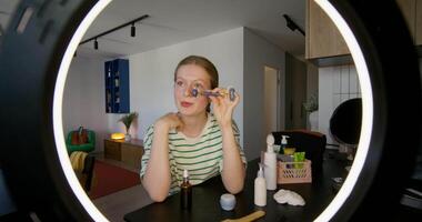 A woman is looking into a mirror while using a makeup brush video