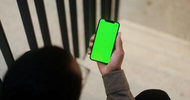 A person holding a green screen phone in front of a person sitting on a stair video