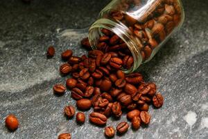 Coffee beans spilling out of a glass jar on a stone background photo