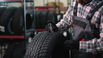 Mechanic checking tire tread depth with gauge in auto shop video