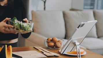 A woman is holding a salad in front of a tablet video