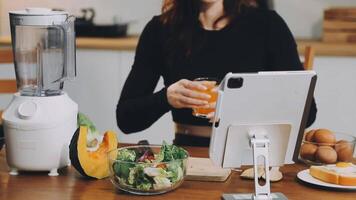 A woman is sitting at a table with a tablet and a blender video