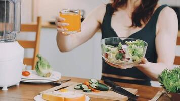 un mujer participación un vaso de jugo mientras sentado a un mesa con un ensalada y un licuadora video