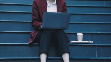 A woman in a business suit sitting on the steps of a building with a laptop video