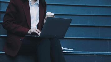 A woman in a business suit sitting on steps with a laptop video