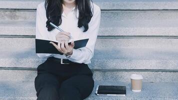 A woman sitting on the steps with a notebook and coffee video