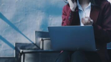 A woman in a business suit sitting on steps with a laptop video