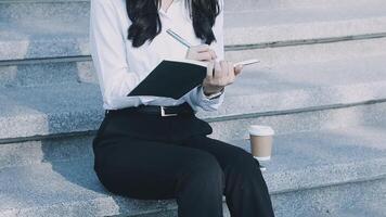 A woman in a business suit sitting on steps with a notebook and coffee video