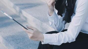 A woman in a business suit sitting on steps with her tablet video