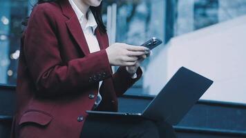 A woman in a business suit sitting on steps with her laptop video