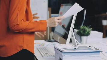 A woman is holding a piece of paper while standing in front of a computer video