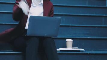 A woman in a business suit sitting on some stairs with a laptop video