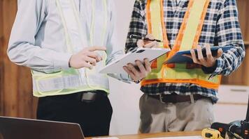 Two construction workers standing at a desk with a tablet video
