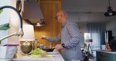 A bald man in glasses is preparing food in a kitchen video