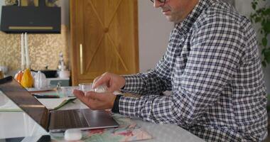 A man in glasses sitting at a table with a laptop video
