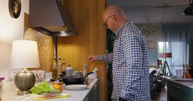 A bald man in a checkered shirt is cooking in a kitchen video