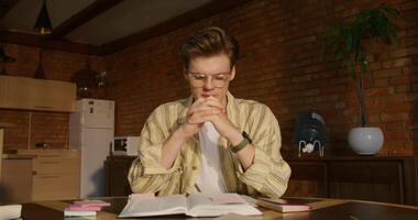 A man in glasses sits at a table with a book and a pen video