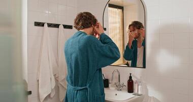 A man in a bathrobe is looking in the mirror video