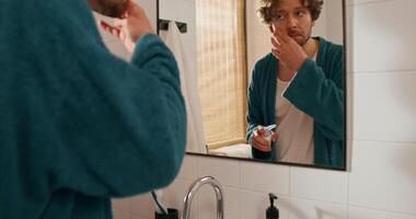 A man in a bathrobe brushing his teeth in front of a mirror video