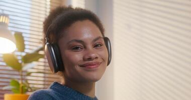 uma mulher com fones de ouvido é sorridente às a Câmera sentado dentro de casa, fechar-se do dela face video