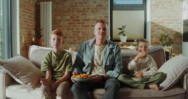 A man and two boys sitting on a couch eating popcorn video
