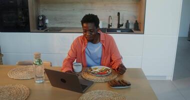 A man sitting at a table with a laptop and food video