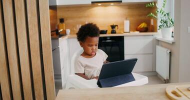 A little girl sitting in a high chair using a laptop video