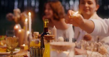 Guests smile and talk while sitting at a beautifully served festive table in the open air. Close-up of a man's hand lighting a candle video
