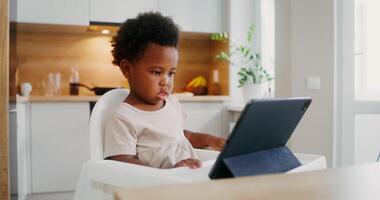 A young child sitting in a high chair using a laptop video