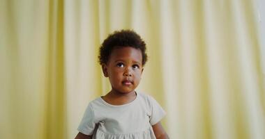 A cute little girl of African-American appearance sits on a chair with a serious look, and then begins to smile video