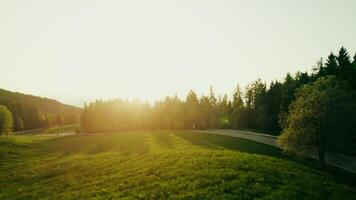 Green mountain valley at dawn. Fields and hills flooded with sunlight, a bird's-eye view from a drone video