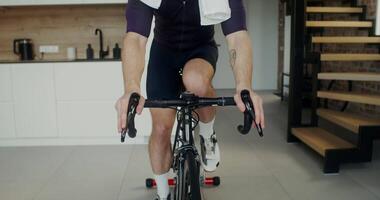 A young man in headphones with a towel around his neck looks at the camera while using an exercise bike, dynamic from a man's hands on the handlebars of a bicycle to his face video