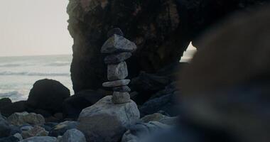 A pyramid of stones is built on the seashore near a rock video