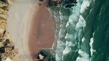 The drone circles around a sandy beach surrounded by rocks and washed by sea waves video