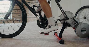 A young man of European appearance is exercising on an exercise bike in a modern home interior. Movement of the from the man's legs to his face, close-up video
