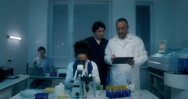 Two people in lab coats looking at a tablet video