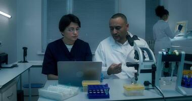 Two people in lab coats looking at a laptop video