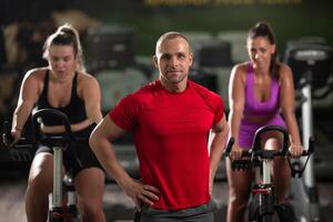 A determined fitness trainer standing confidently in front of his two female clients, guiding them through their workout in the background. photo