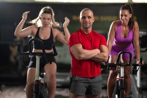 A determined fitness trainer standing confidently in front of his two female clients, guiding them through their workout in the background. photo