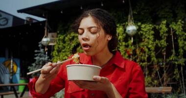 A woman eating a bowl of noodles in front of a building video