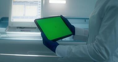 A person in a lab coat holding a tablet with a green screen video