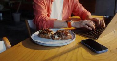 A man sitting at a table with a plate of food and a laptop video
