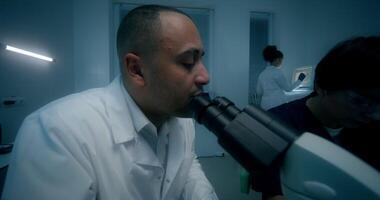 A man in a lab coat looking through a microscope video