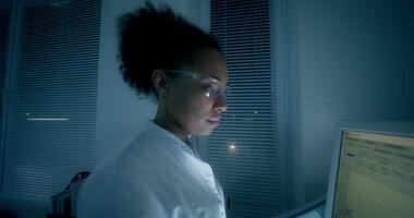 A woman in a lab coat is looking at a computer screen video