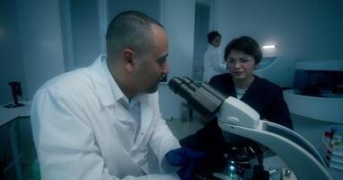 A man and woman in a laboratory looking at a microscope video